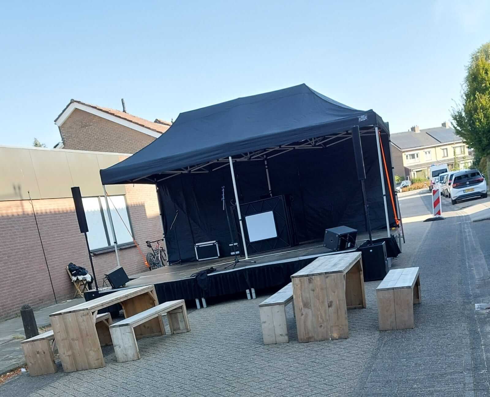 Mobiel podium met geluidsinstallatie en houten zitmeubilair, klaar voor een buitenfeest